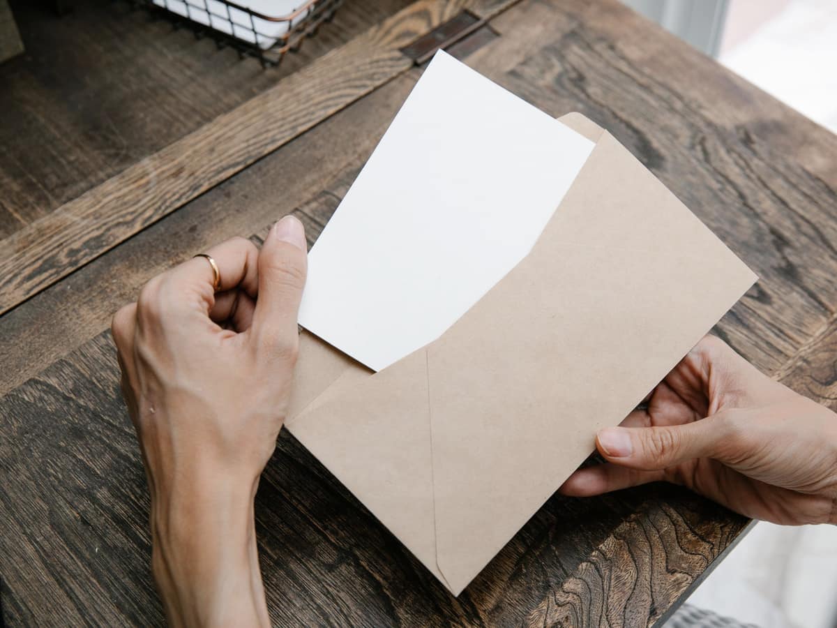 Hands pulling a letter out of an envelope on a wooden desk, seen from above