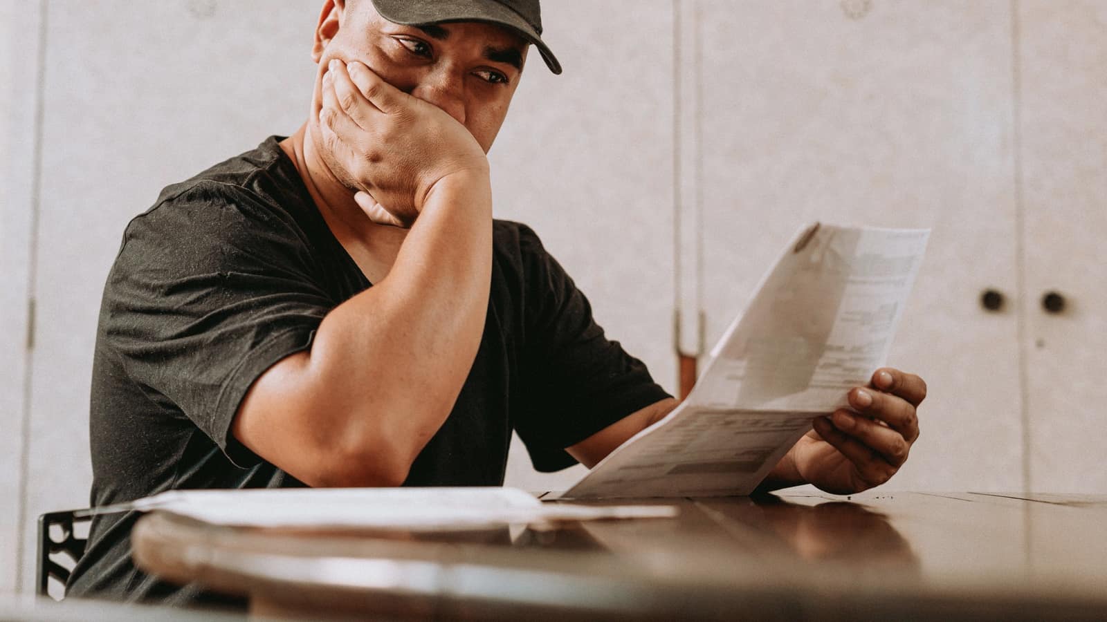 A man at his kitchen table reads a claim statement with his hand over his mouth